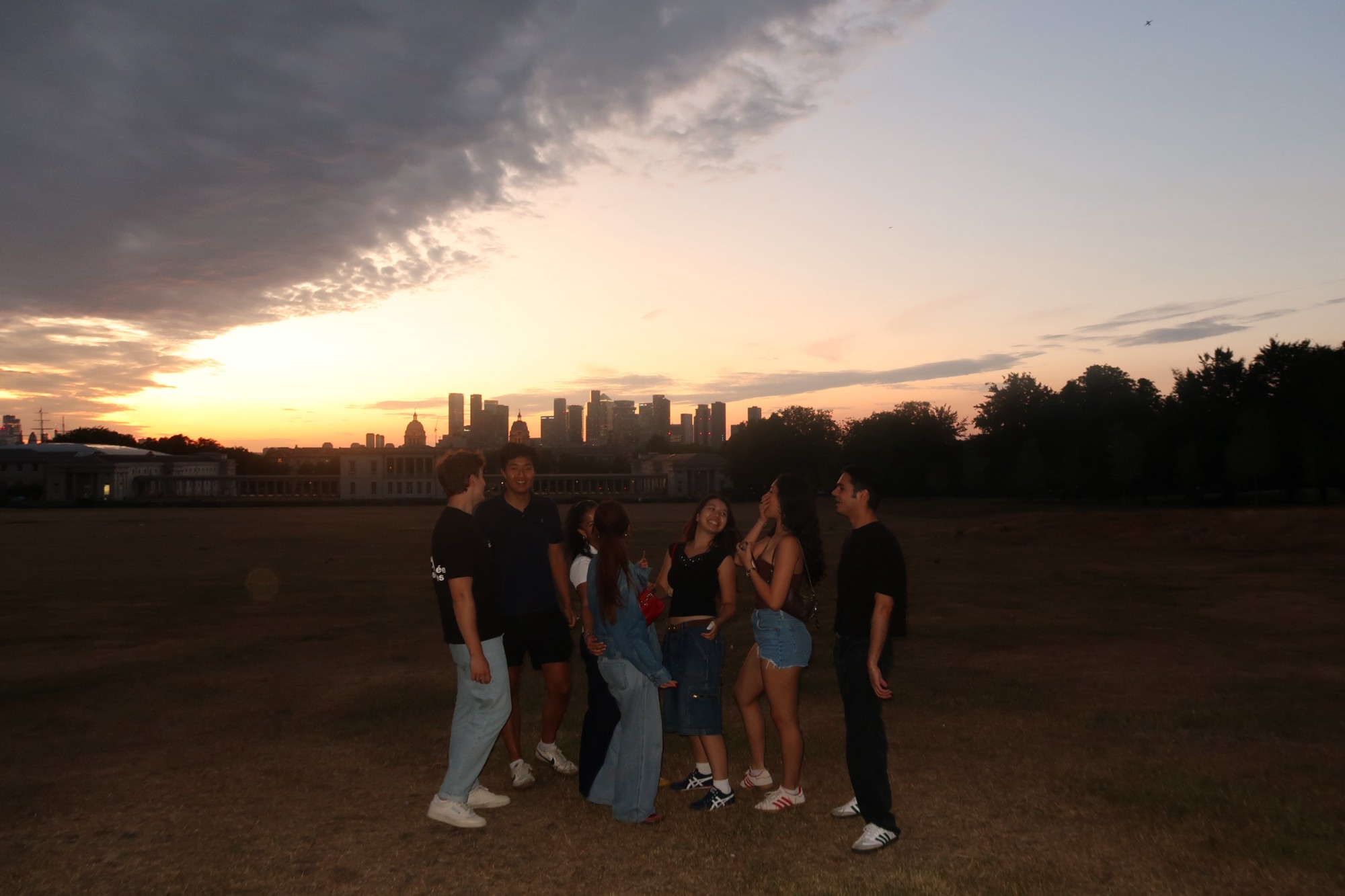 Friends in Greenwich Park at dusk, with the London skyline behind